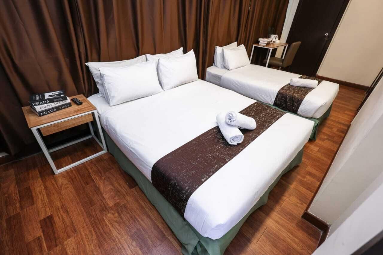 Une chambre d’hôtel avec deux lits, une table de chevet en bois sur laquelle sont posés des livres, et une petite table.