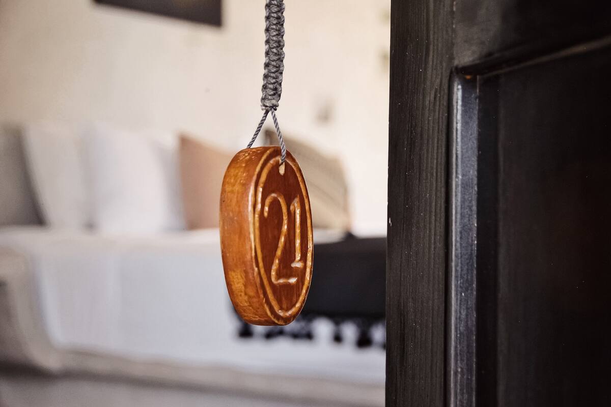 A wooden number plaque hanging from a rope, with a blurred background of a bed and pillows.