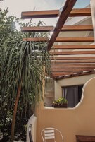 A wooden pergola with a hanging plant, a white chair, and a small table with a potted plant.