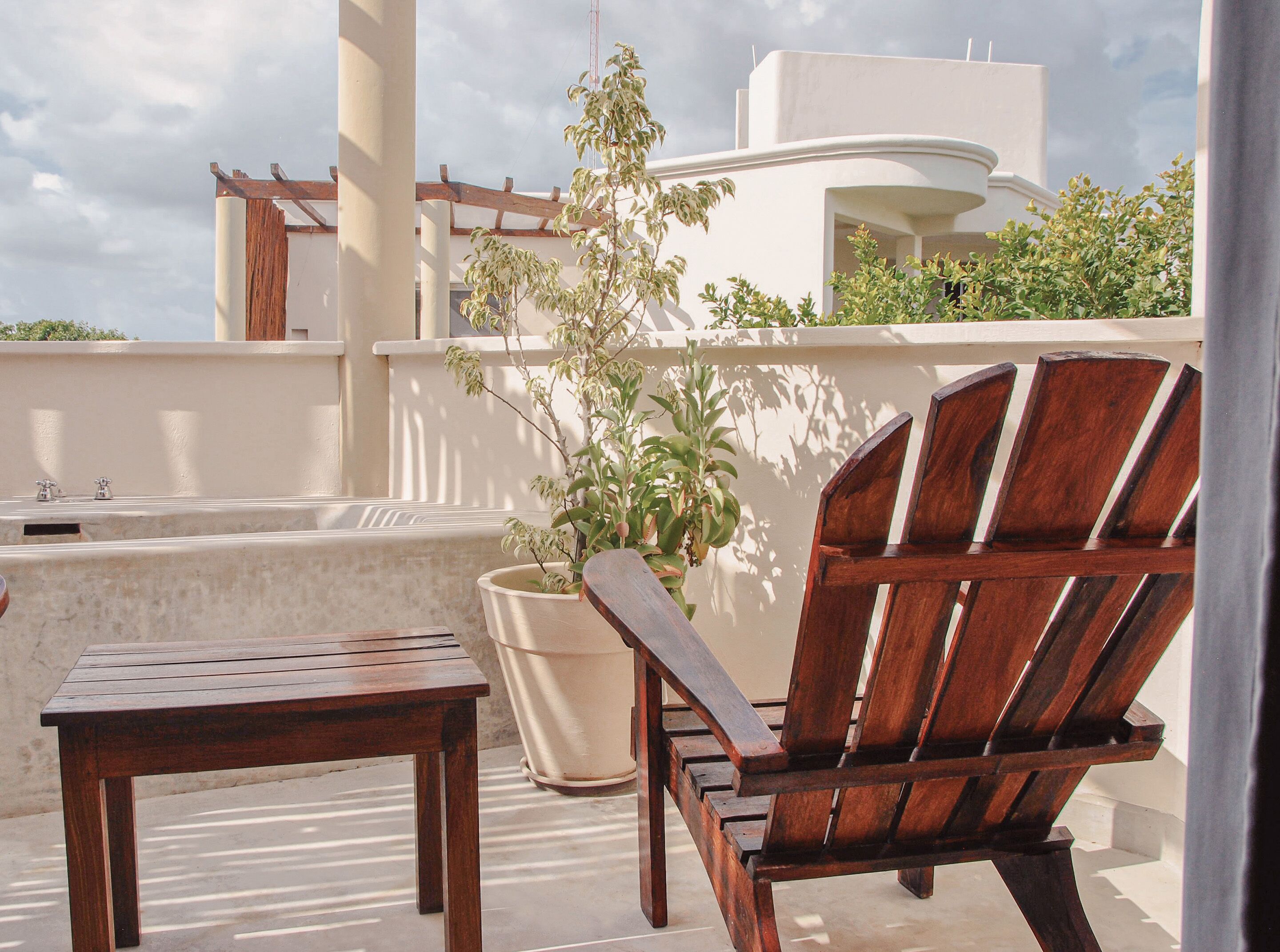 A wooden chair and table on a balcony with a potted plant and a bathtub.