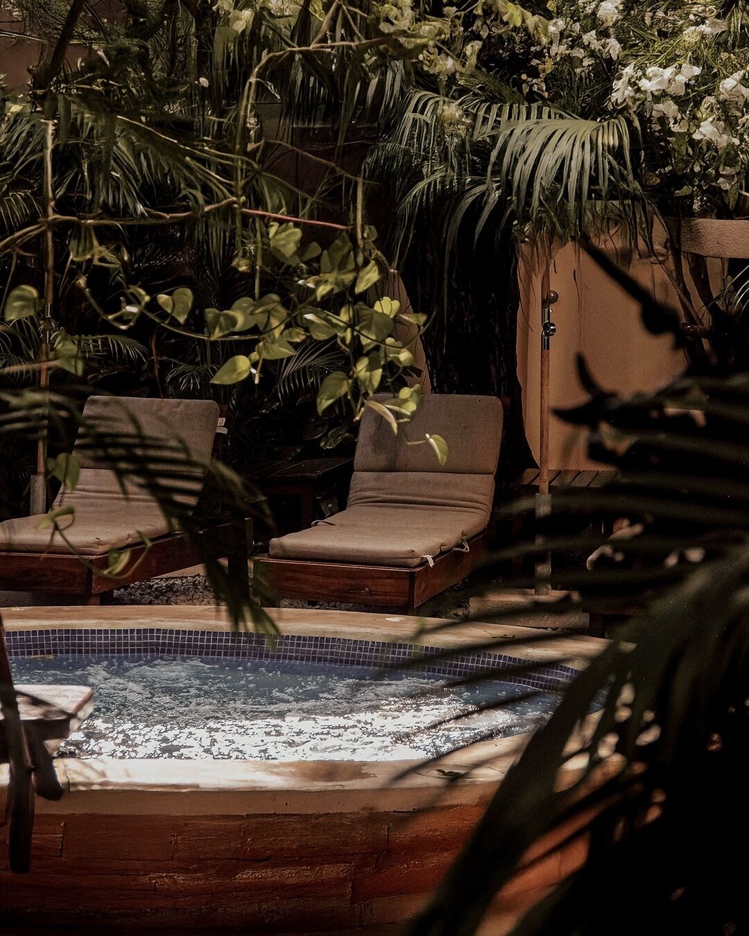 A hot tub surrounded by lush greenery and a tiled pool area.