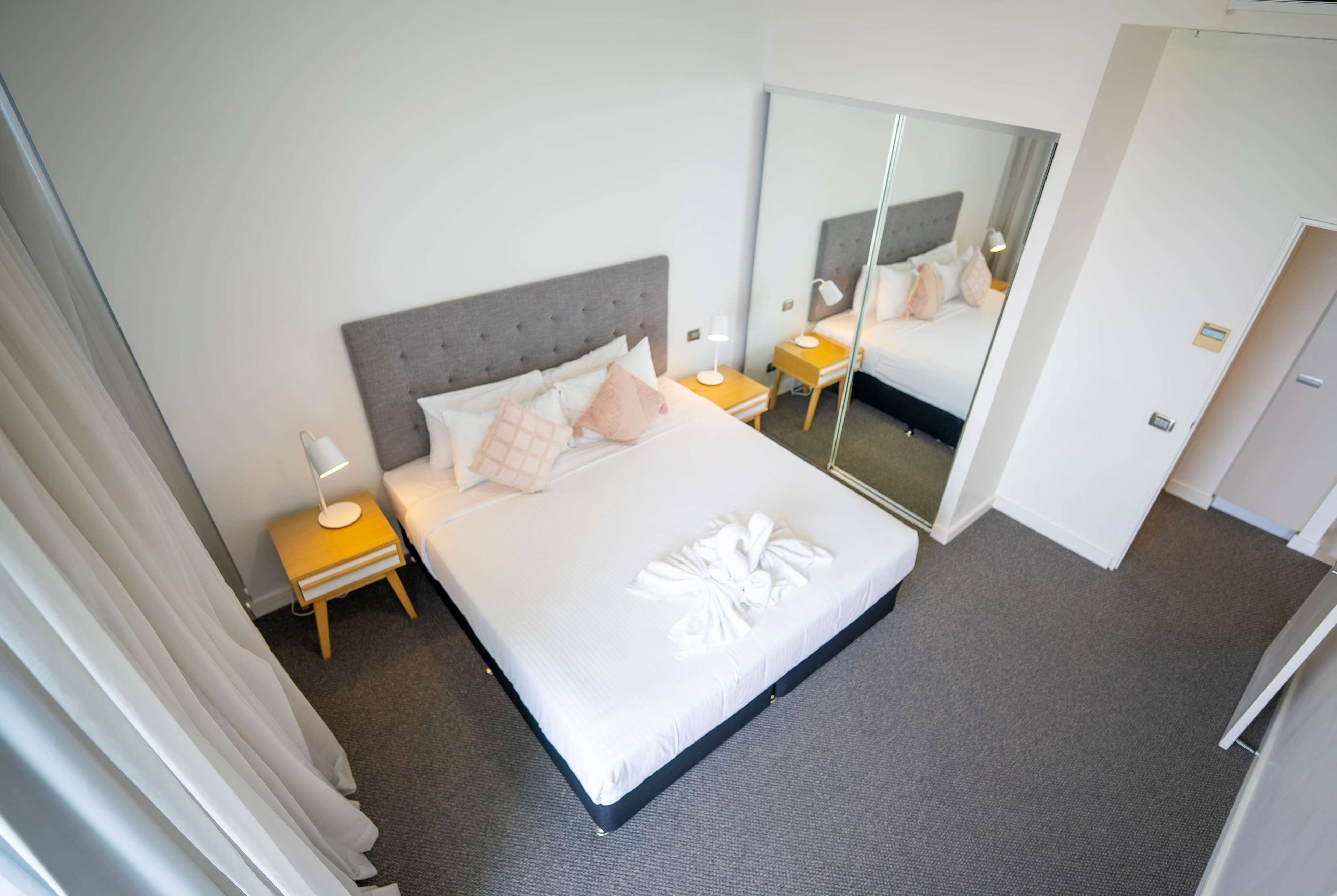 A neatly made bed with a grey headboard, a bedside lamp, and a mirror on the wall.