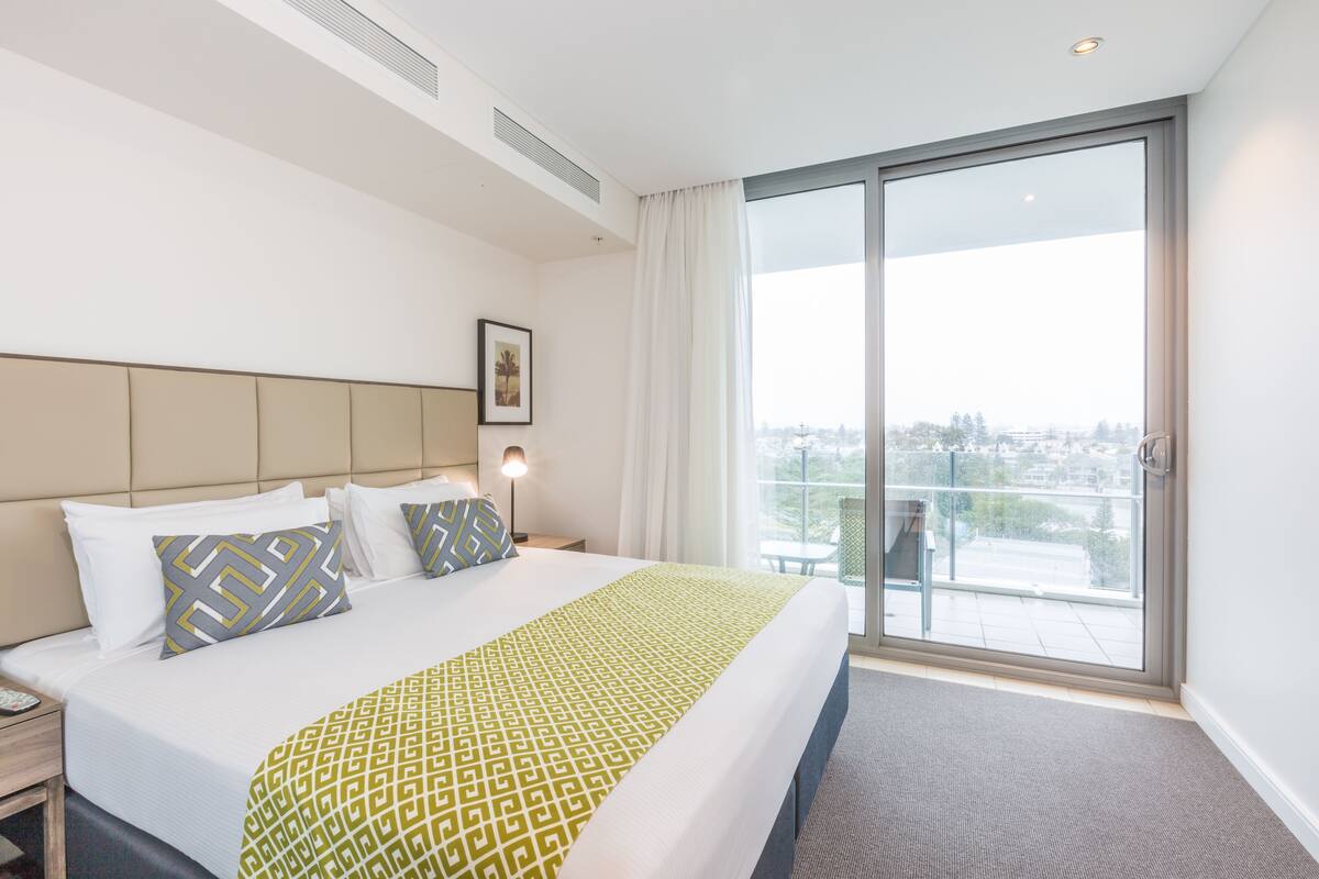 A hotel room with a large bed, a view of the city through a sliding glass door, and a balcony.