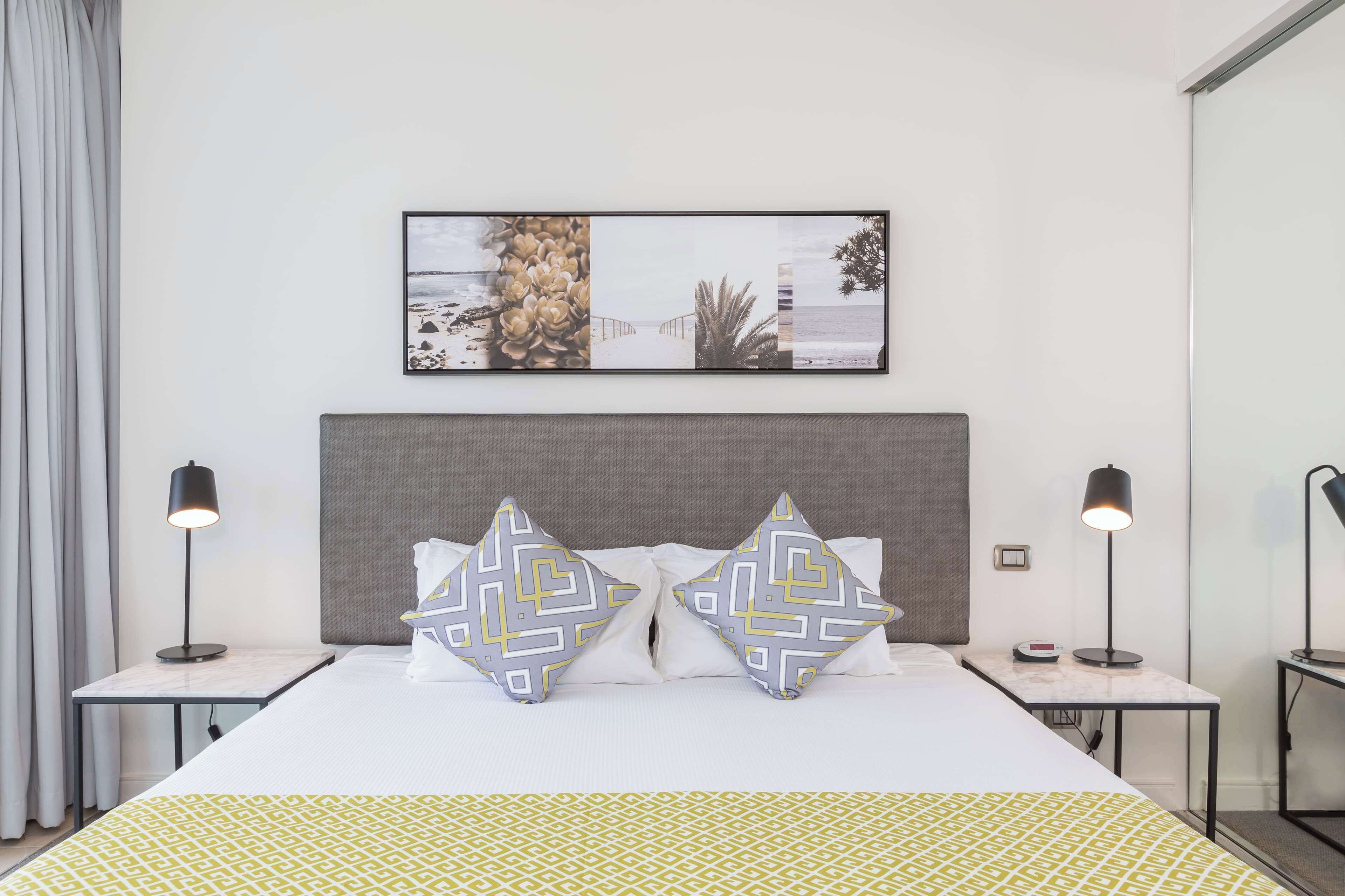 A neatly arranged hotel room with a large bed, two bedside tables with lamps, a framed picture on the wall, and a patterned bedspread.