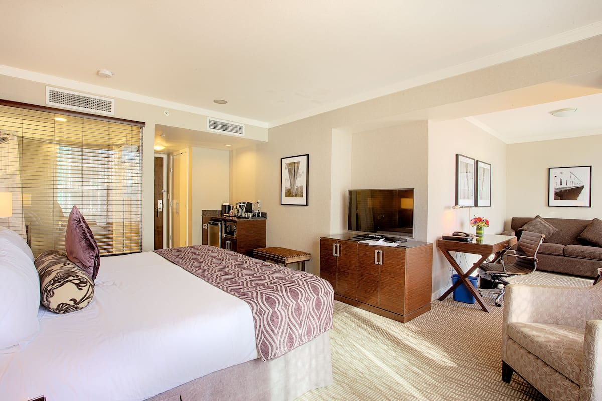 A hotel room with a large bed, a desk with a computer, a sofa, and a TV.