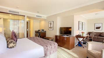A hotel room with a large bed, a desk with a computer, a sofa, and a TV.