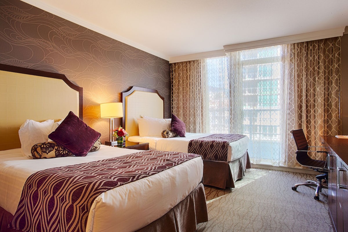 A hotel room with two beds, a desk, and a chair.