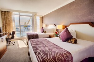 Habitación de hotel con dos camas, un escritorio y vistas a la ciudad.