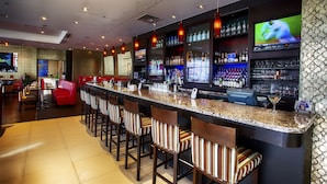 A bar area with a long counter, multiple stools, and a television screen displaying a sports event. - Pinnacle Hotel at the Pier (North Vancouver)