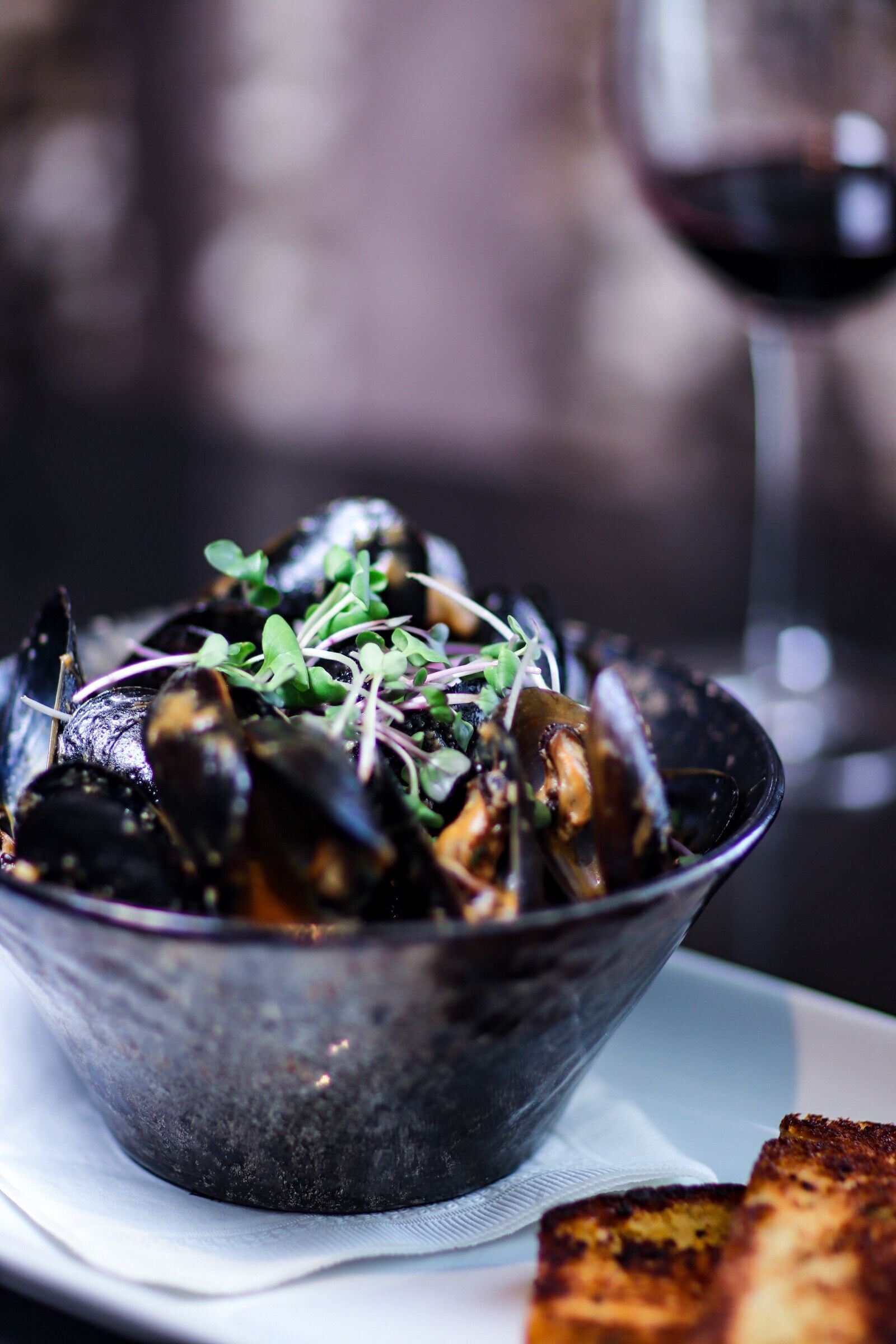Un bol de moules accompagnées de légumes verts et un verre de vin rouge sur une table.