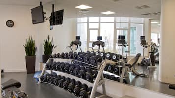 A gym with exercise equipment, a mirror, and a clock on the wall.