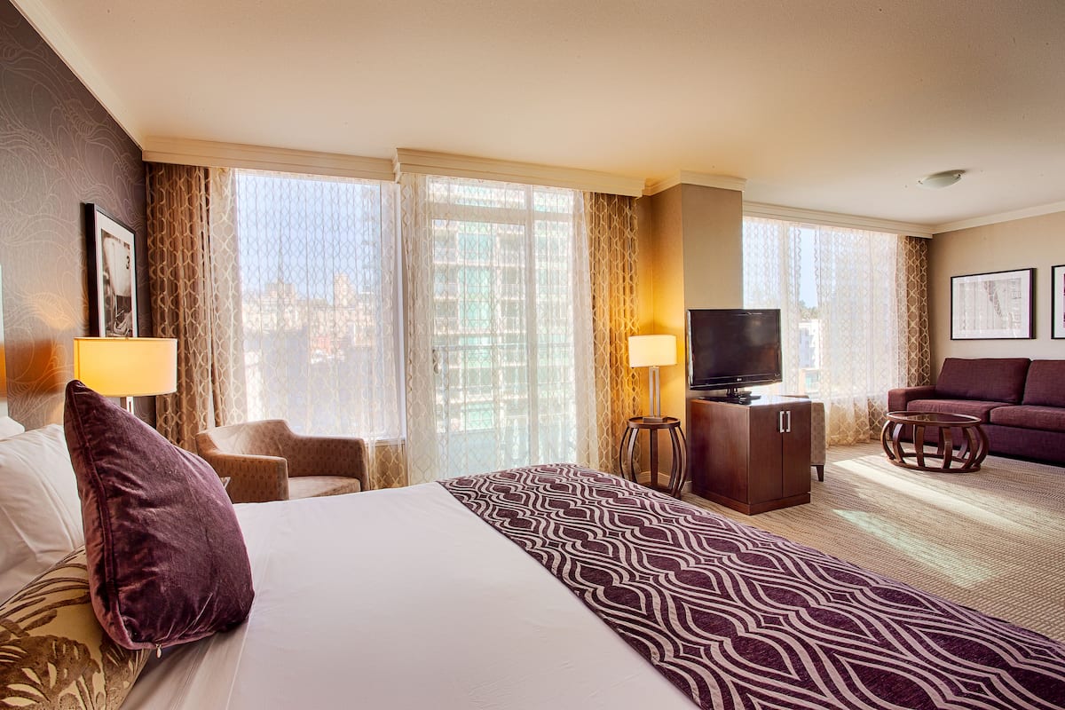 A hotel room with a large bed, a TV, a sofa, and a desk with a lamp.