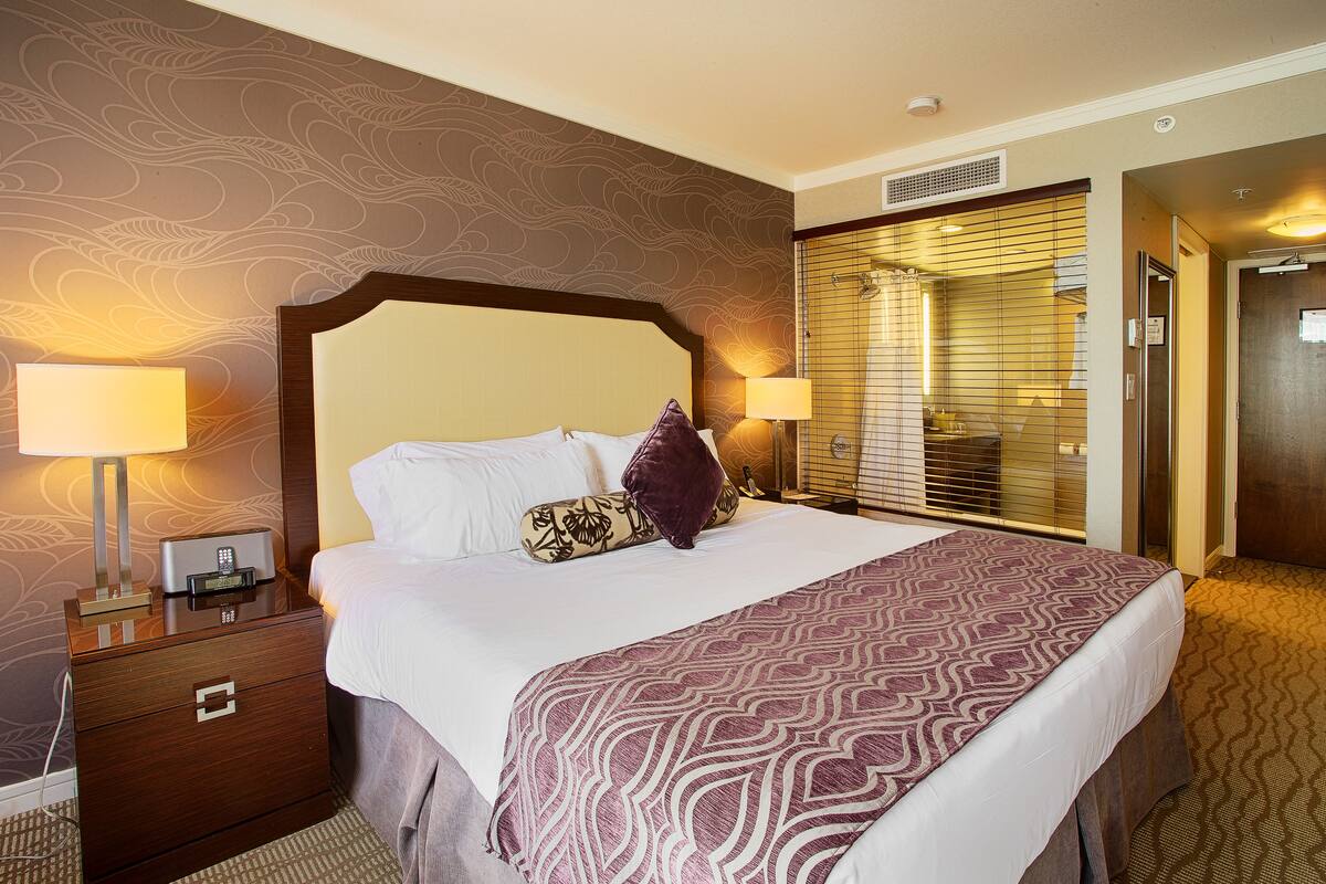 A hotel room with a large bed, two bedside tables with lamps, a wooden headboard, and a patterned wall.