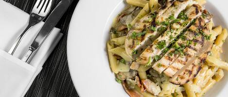 A plate of grilled chicken and pasta with a fork and knife on a black tablecloth.