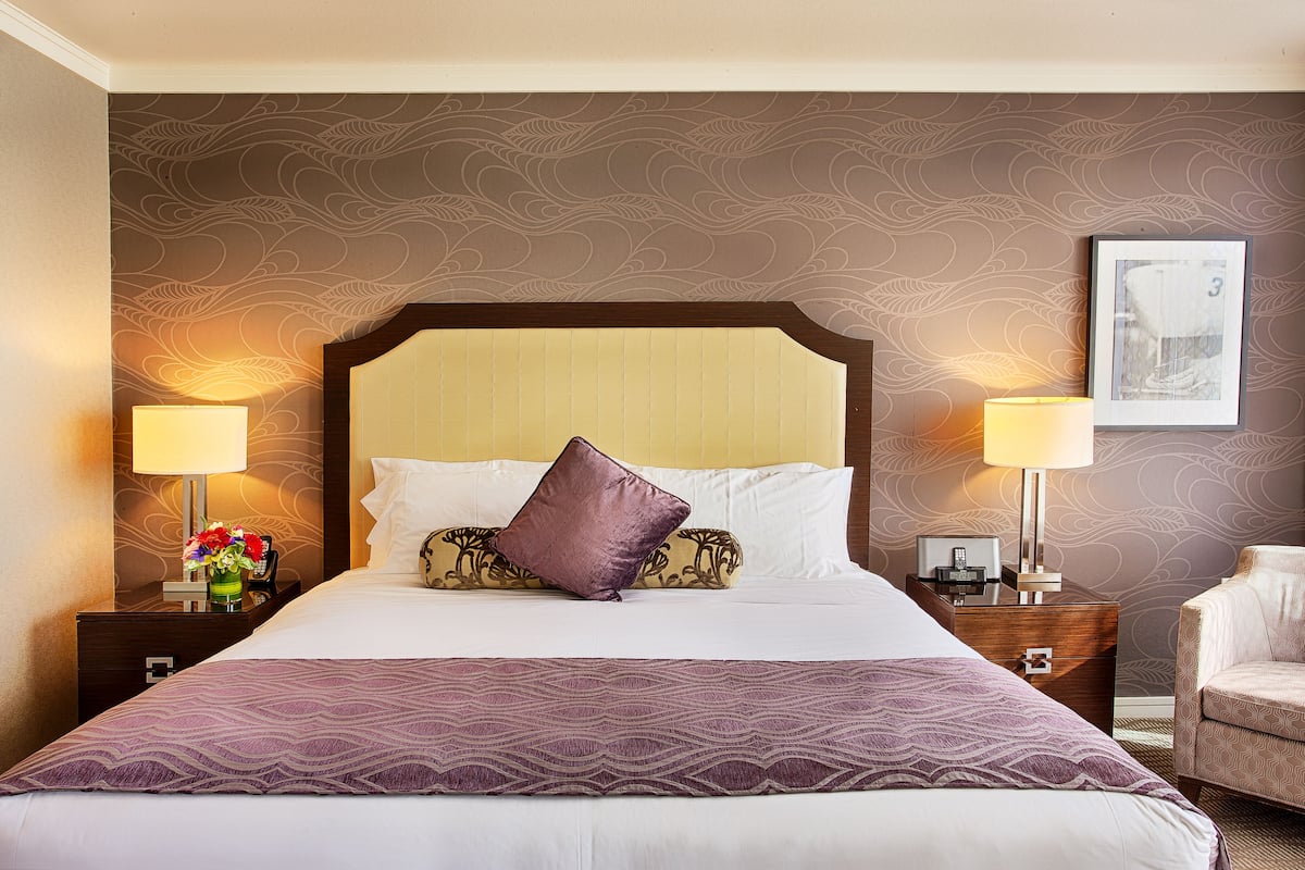 A hotel room with a large bed, two bedside tables, a nightstand, a chair, and a wall with a decorative pattern.