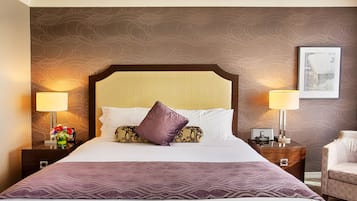 Una habitación de hotel con una cama grande, dos mesitas de noche, un sillón y una pared con un diseño decorativo.