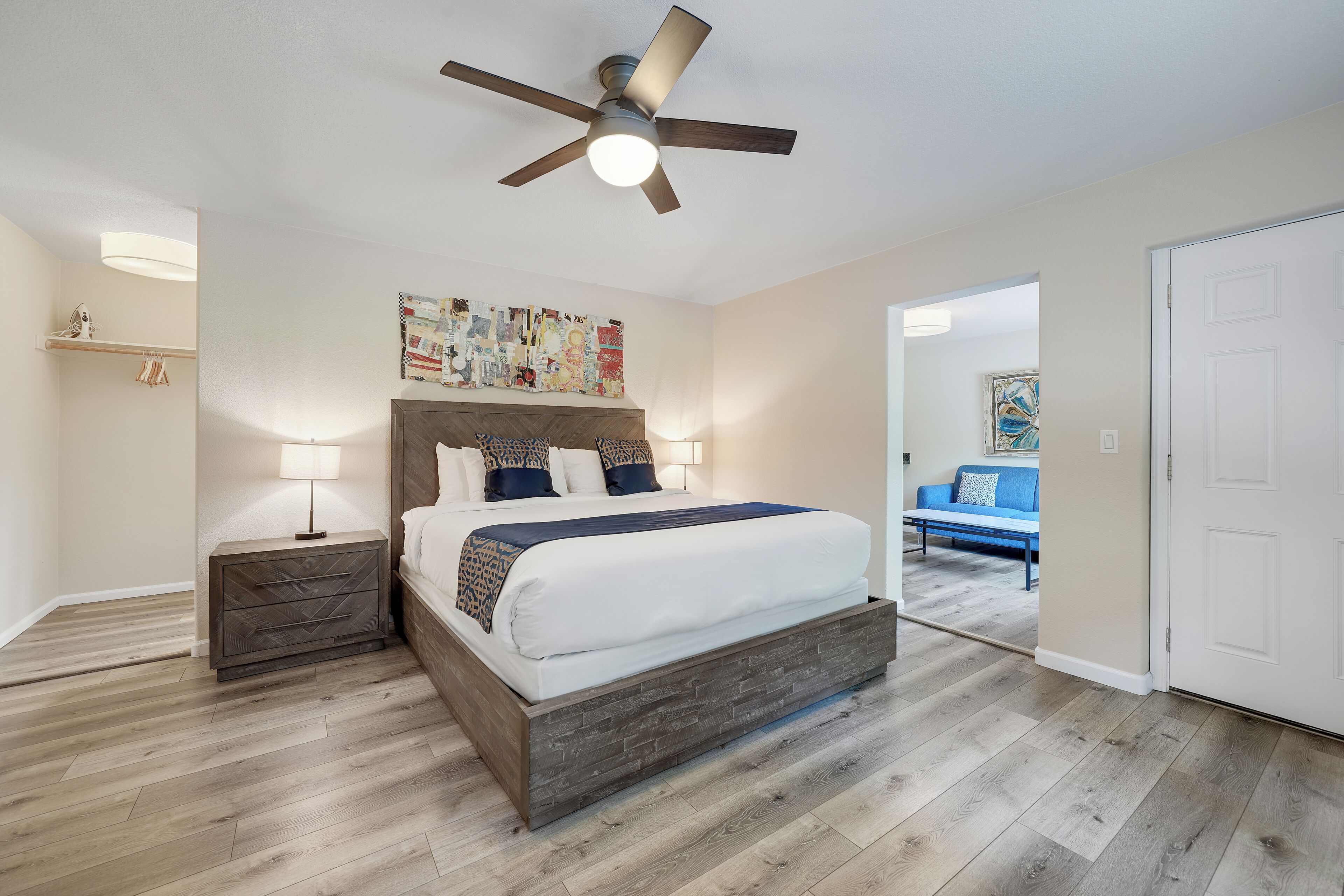 Un dormitorio con cama, mesitas de noche, ventilador de techo y una obra de arte en la pared.