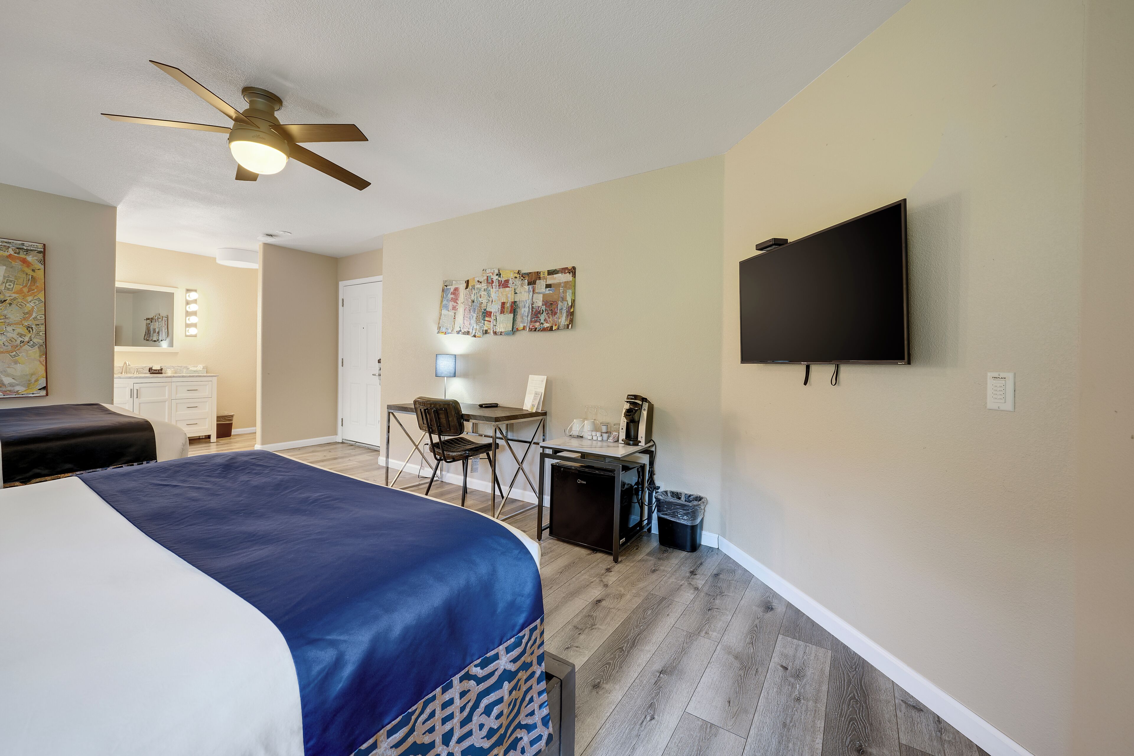 A hotel room with a bed, a desk, a chair, a television, and a ceiling fan.