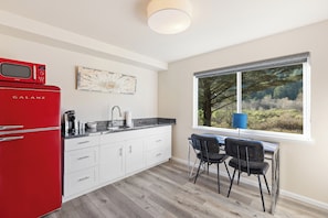 A modern kitchen with a red Galanz refrigerator, white cabinets, a black countertop, a sink, and a dining area with two chairs.