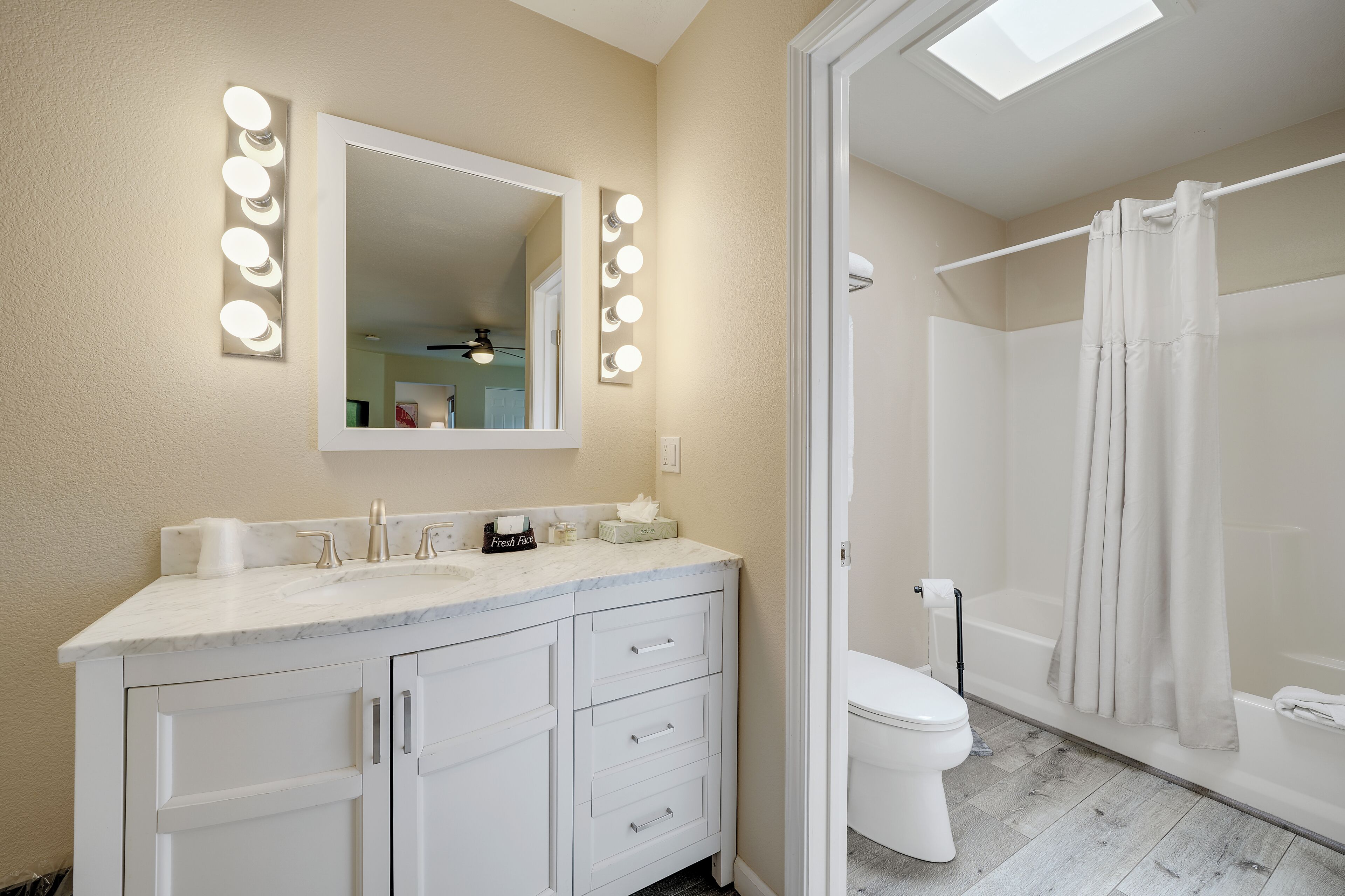 A bathroom with a vanity, a mirror with lights, a toilet, and a shower area.