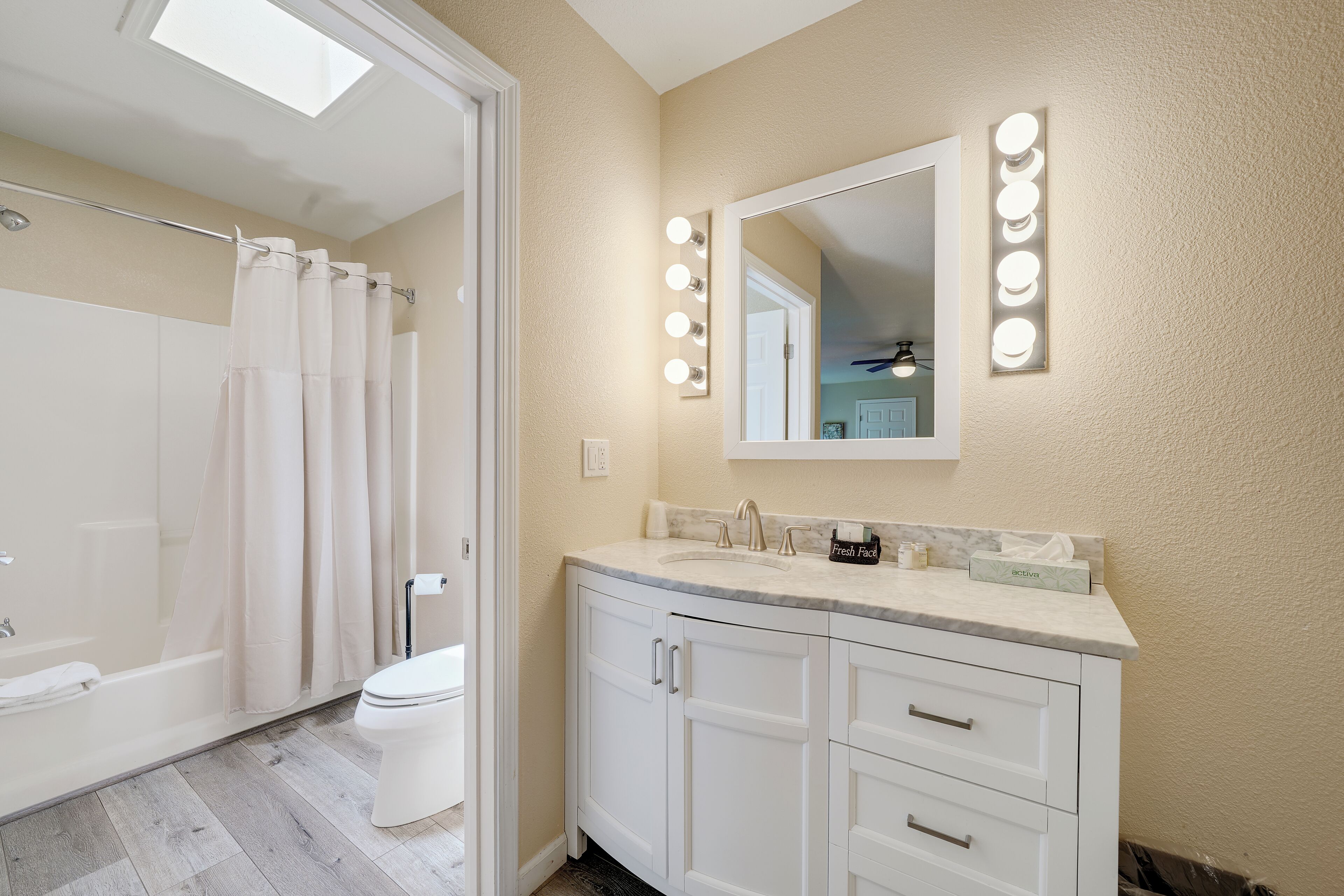 A bathroom with a shower, toilet, vanity with a mirror, and lights.