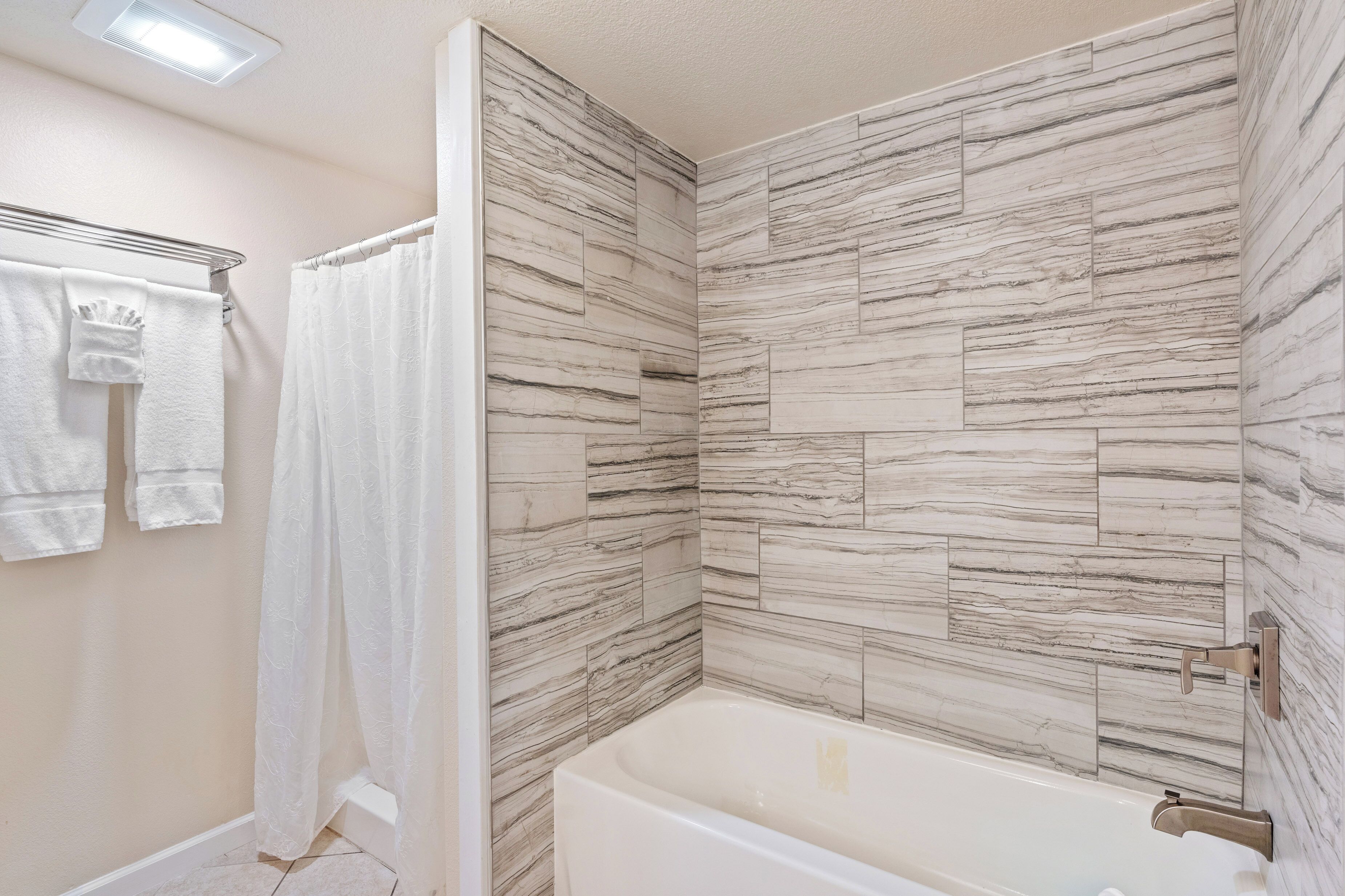 A bathroom with a bathtub, a shower curtain, and a towel rack with towels.