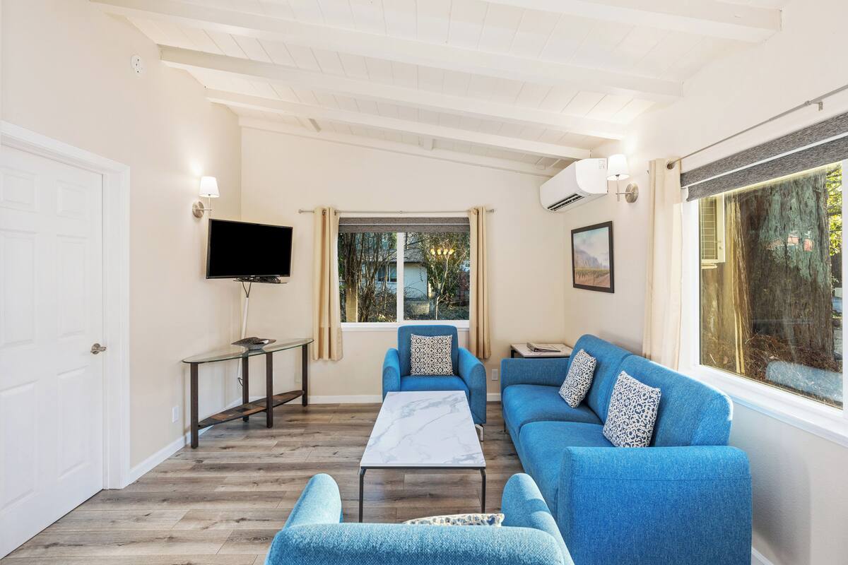 A living room with a sofa, a coffee table, a TV, and a window with curtains.