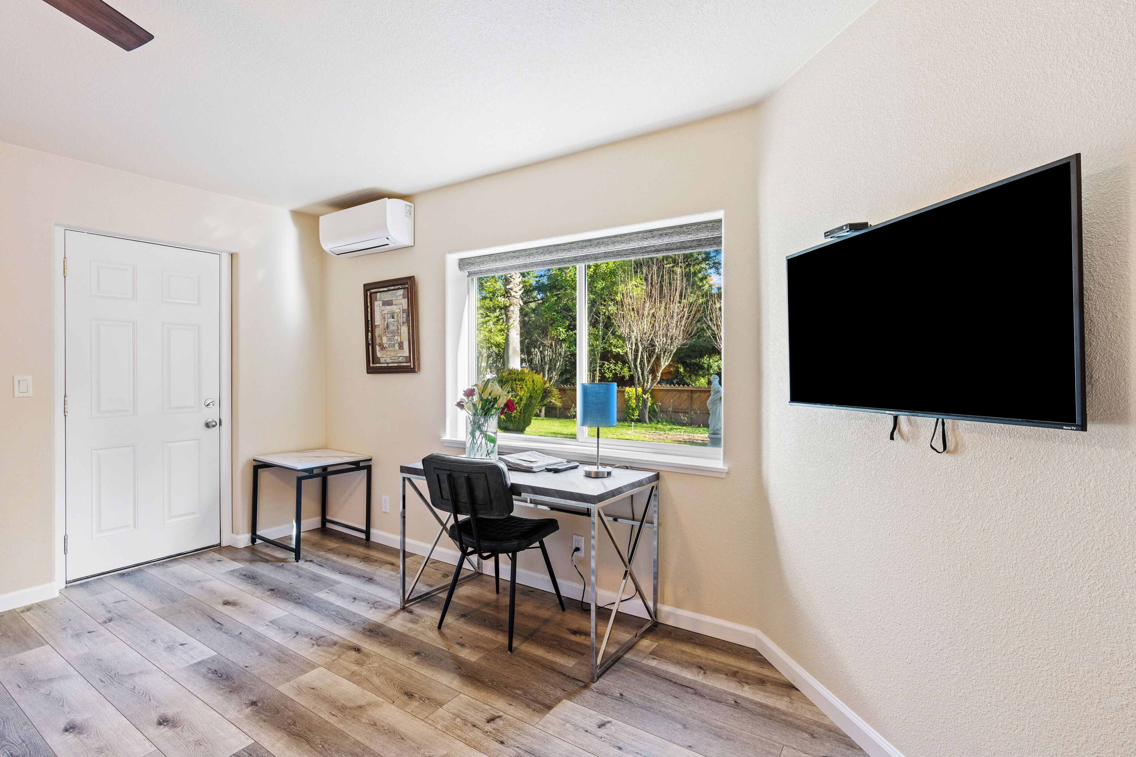 A room with a desk, chair, and a TV mounted on the wall.
