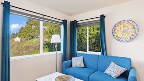 Una habitación con un sofá azul, un cuenco sobre una mesa y vistas al verdor exterior.