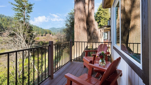Una terraza de madera con dos sillas y una mesa, con vistas a un valle boscoso.