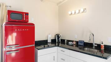 A kitchen with a red Galanz refrigerator, a black countertop, white cabinets, a sink, and a lighted mirror above the countertop.