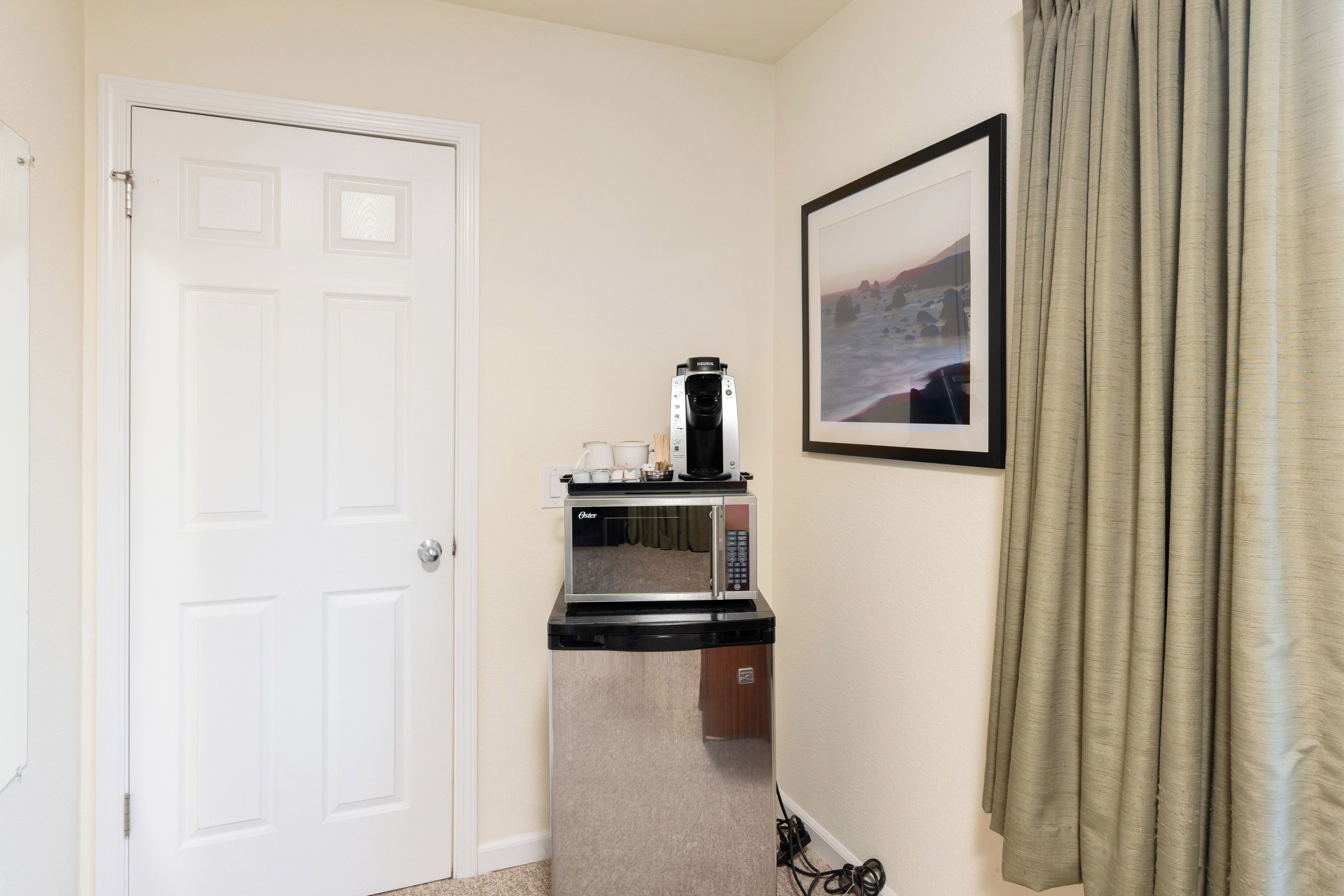Una kitchenette pequeña con microondas, cafetera y un cuadro en la pared.