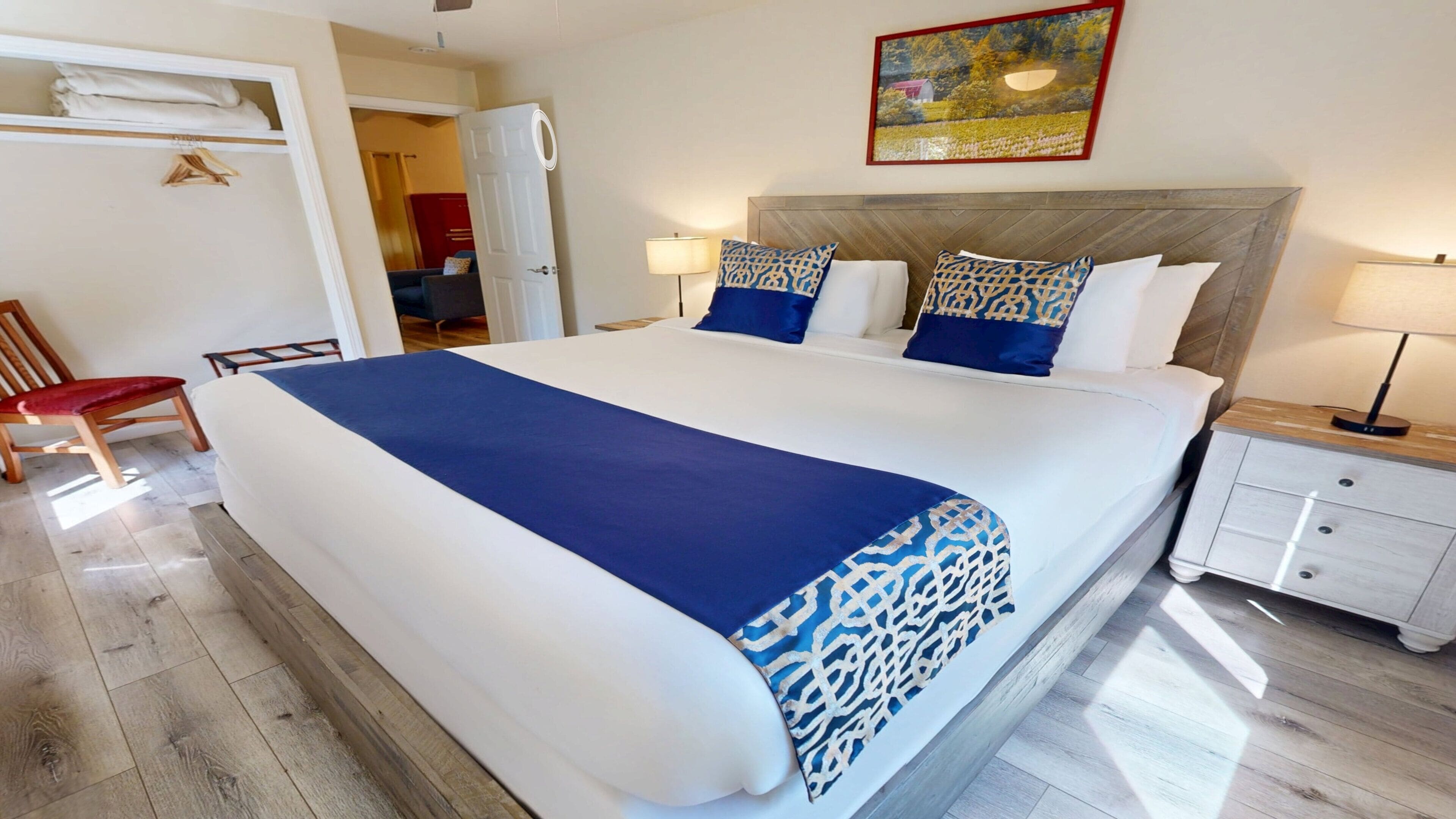 A hotel room with a large bed, a bedside table, a chair, and a wardrobe.