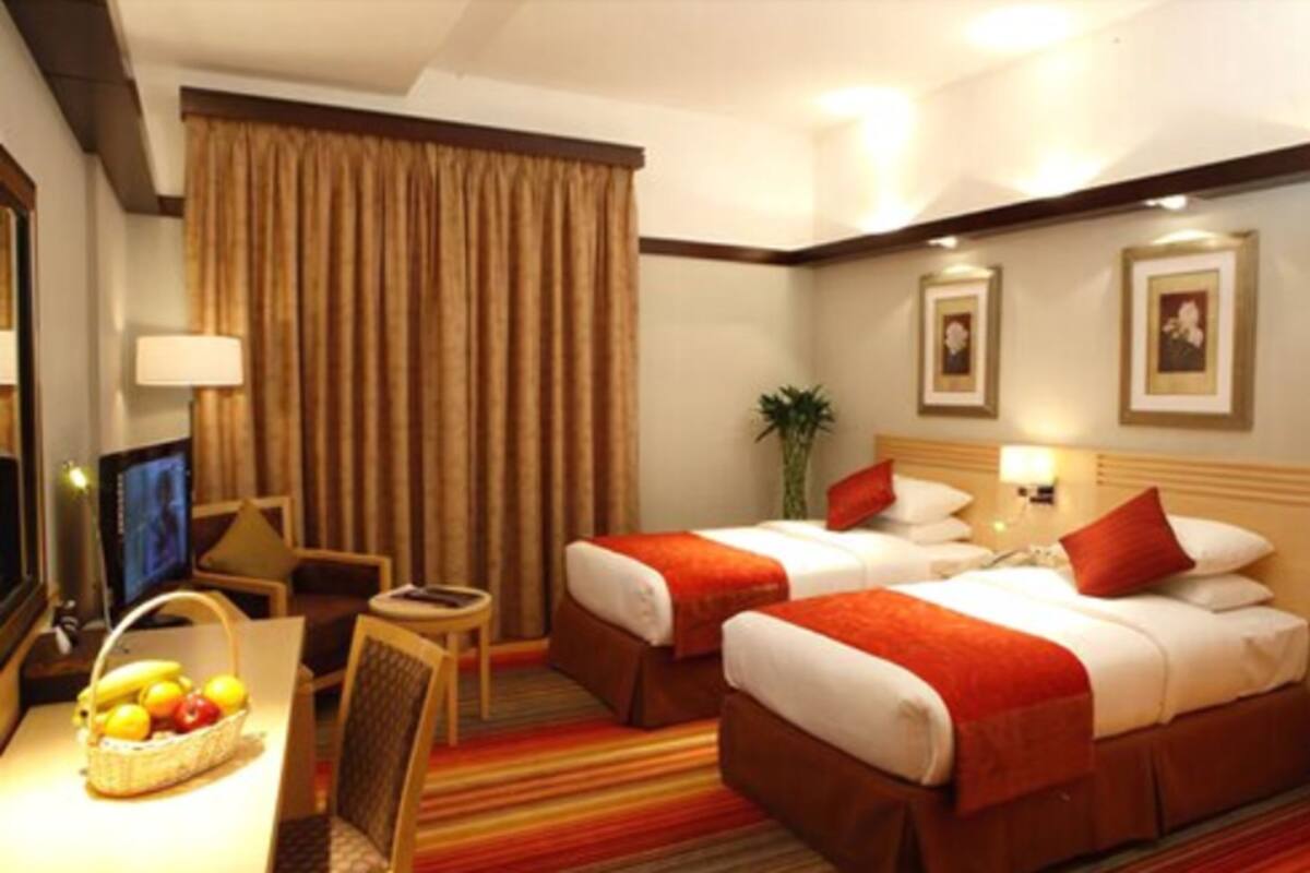 Een hotelkamer met twee bedden, een bureau met lamp, een televisie en een fruitmand.