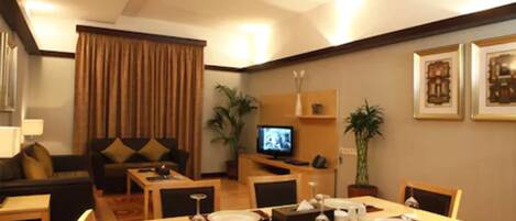 A dining area with a table set for four, a television in the background, and a sofa in the adjacent living area.