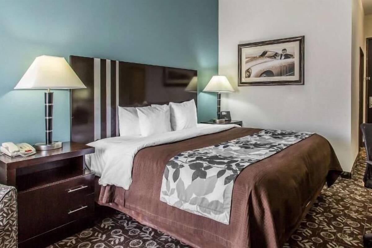 A hotel room with a bed, two bedside lamps, a desk with a phone, a chair, and a door.