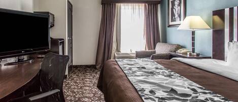 A hotel room with a bed, a desk with a TV, a chair, a lamp, and a window with curtains.
