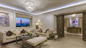 A spacious living room with a large window offering a city view, a chandelier, and a modern fireplace. - Kempinski Nile Hotel Cairo (Cairo)