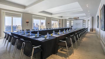 A conference room with a long table, chairs, and city views through large windows.