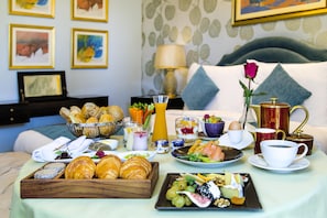 A breakfast buffet with pastries, fruits, and beverages on a table in a hotel room.
