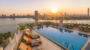 A rooftop pool with lounge chairs and a city skyline view at sunset. - Kempinski Nile Hotel Cairo (Cairo)