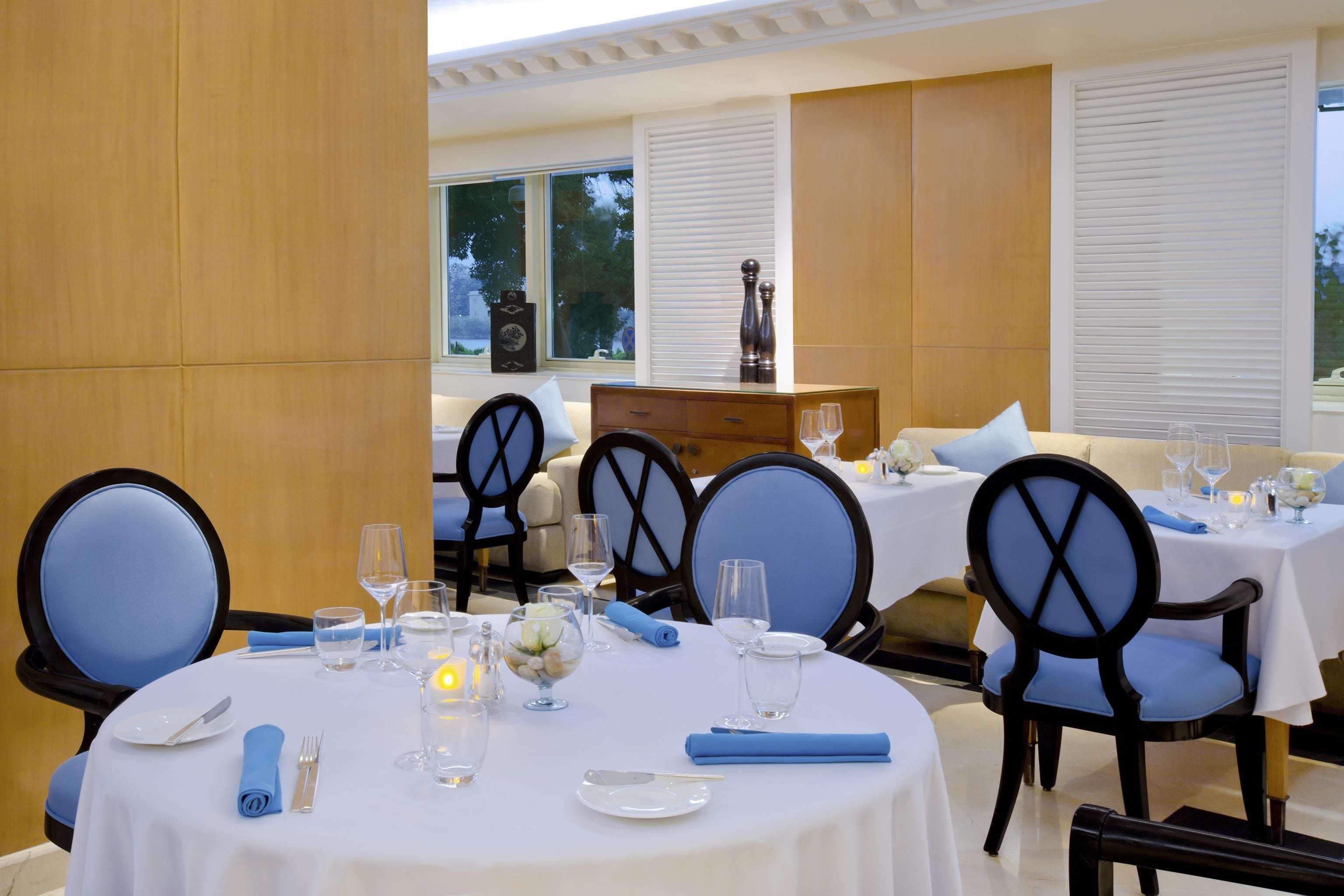 A dining area with round tables, blue upholstered chairs, and white tablecloths.