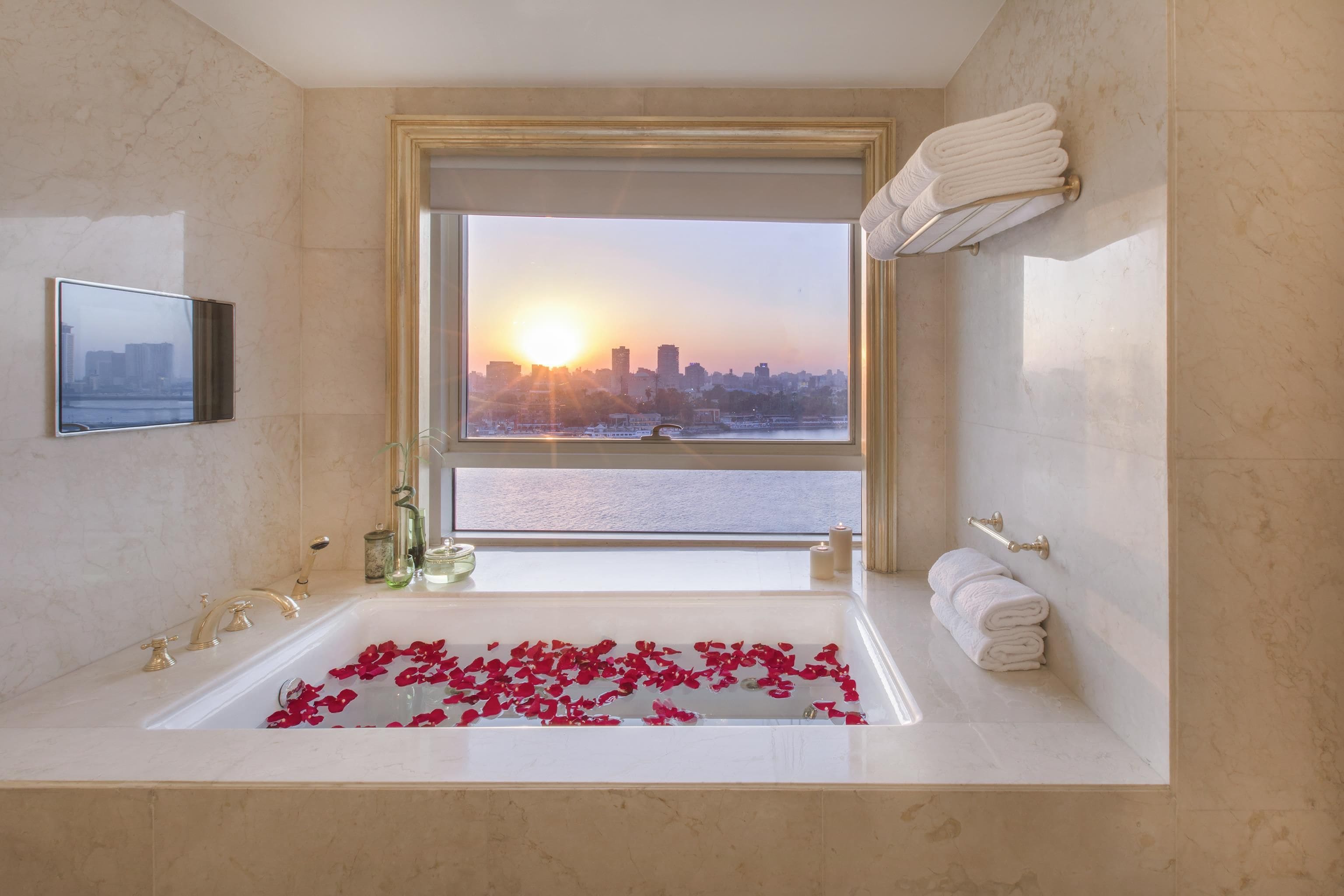 A bathroom with a large bathtub, a window with a cityscape view, and a mirror.