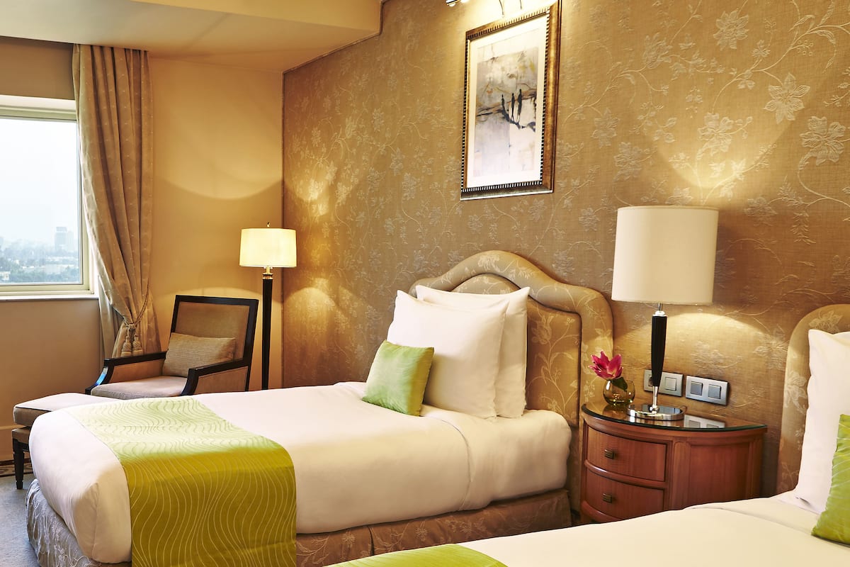 Una camera d'albergo con due letti, un comodino, una sedia e una finestra con tende.