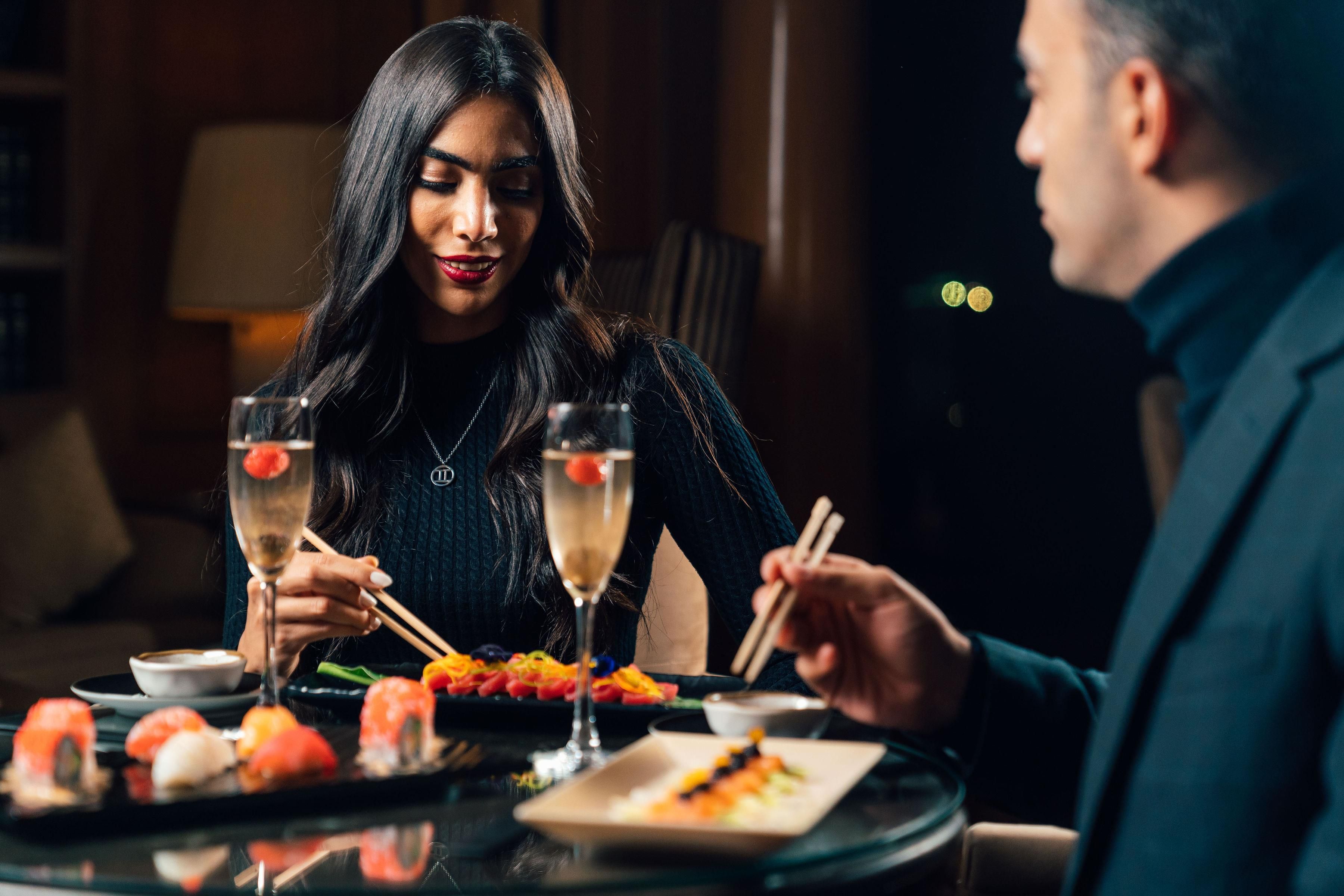 A dining table with sushi, glasses of champagne, and chopsticks.