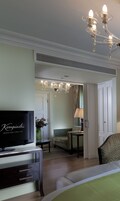 A hotel room with a television, a chandelier, a sofa, a table, and a chair.