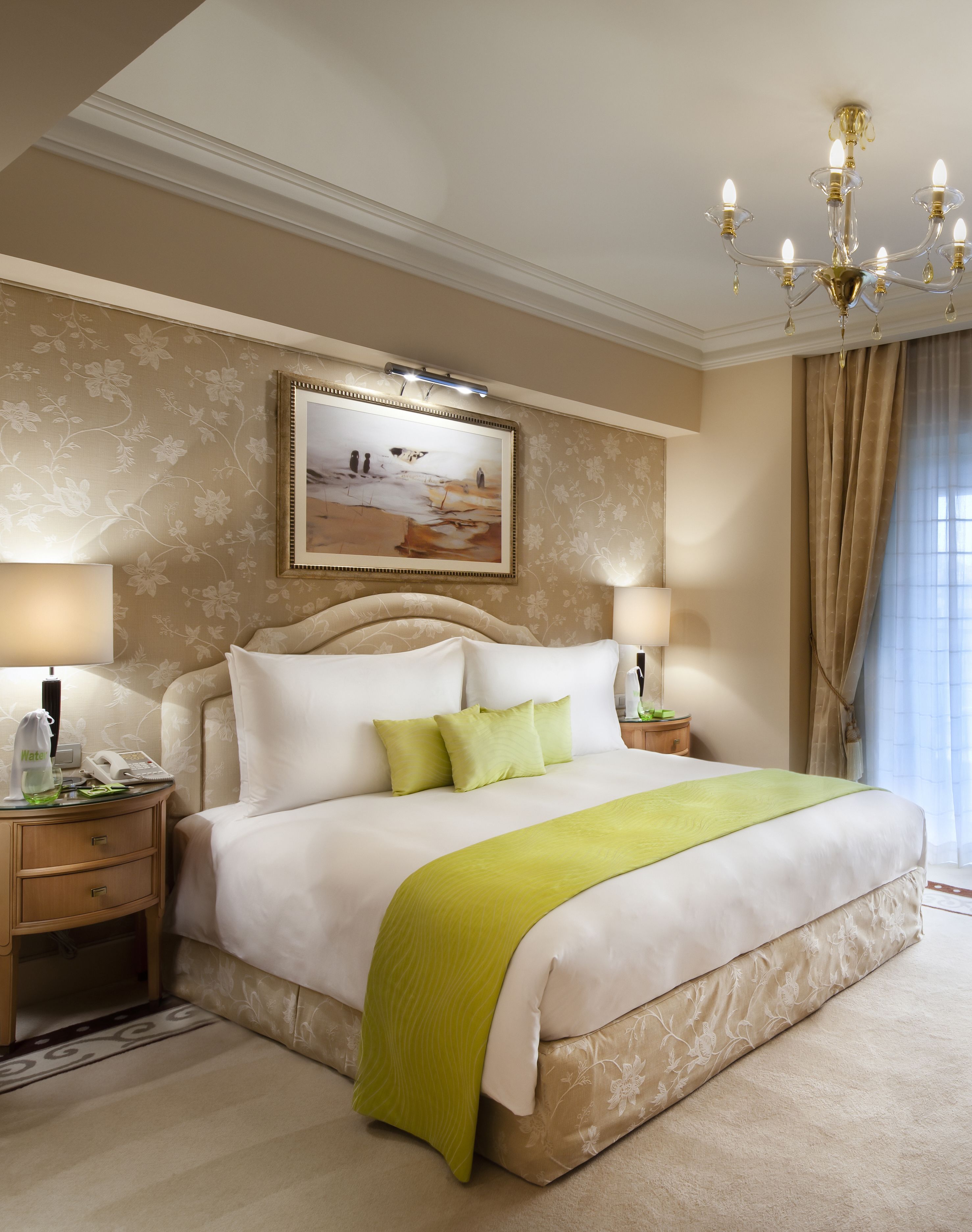 Une chambre spacieuse avec un grand lit, deux tables de chevet, un lustre et un tableau au mur.