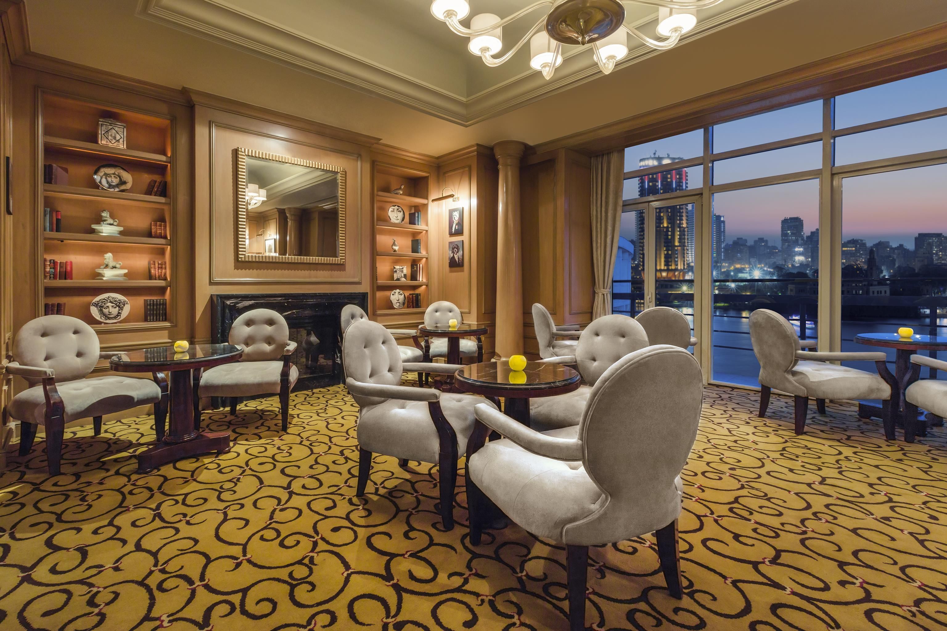 A spacious room with a fireplace, bookshelves, and a large window with a city view.