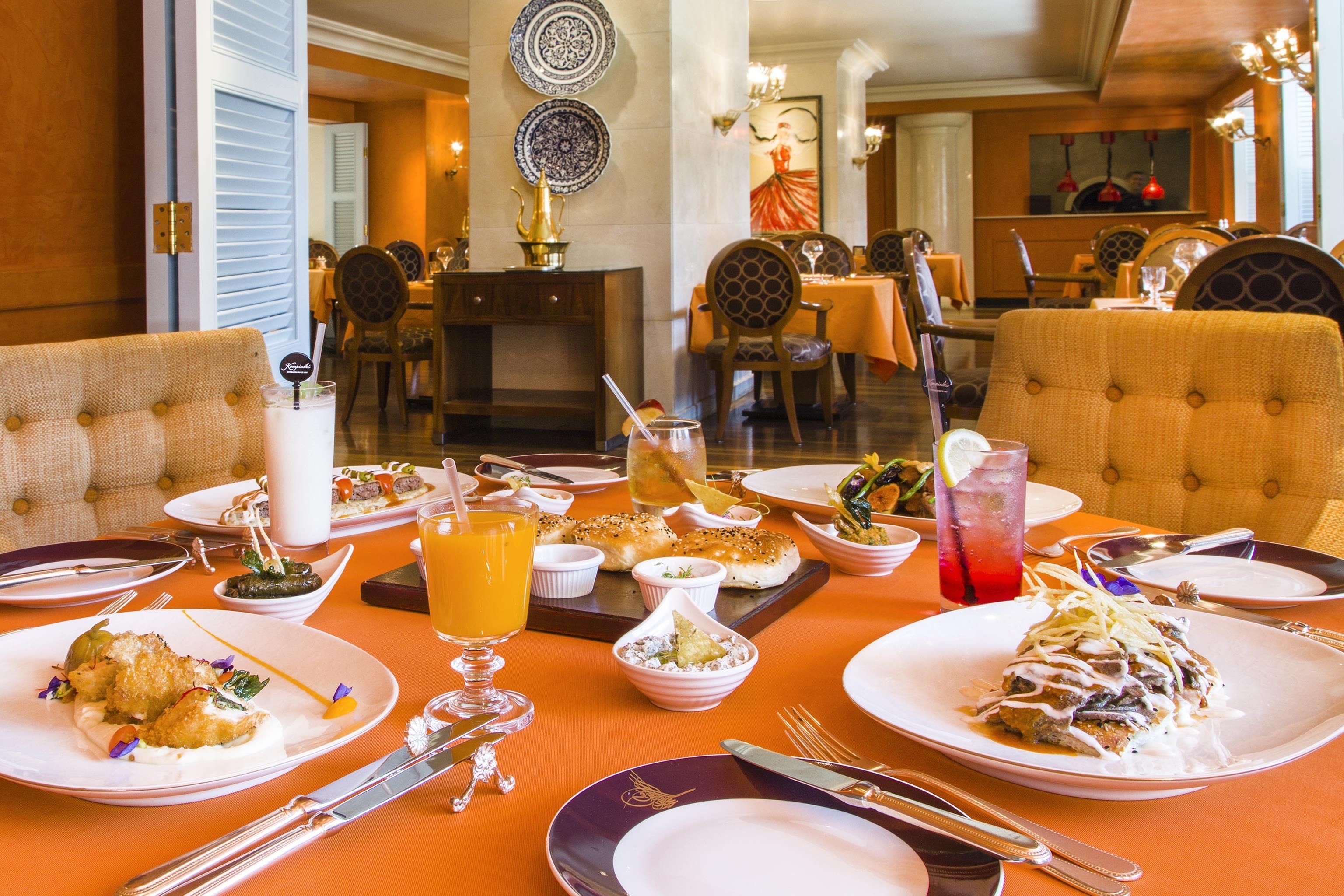 Un comedor con mesas dispuestas para una comida, incluyendo platos, cubiertos y bebidas.