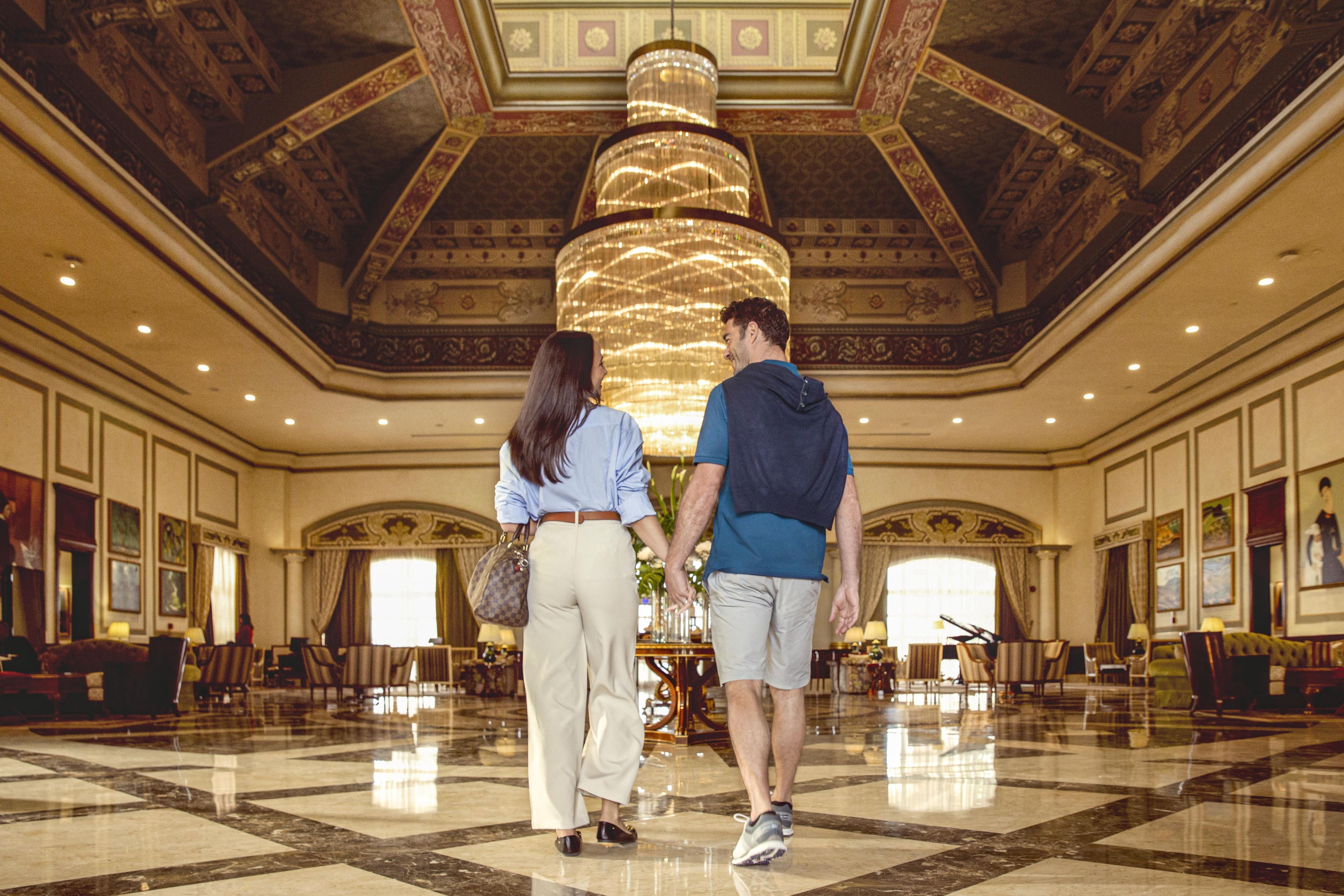 A spacious lobby with a grand chandelier, marble flooring, and classical architecture.